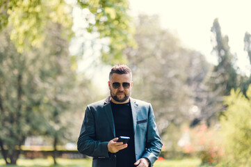 Stylish man in a blue suit in the city. Business style of emotion.Handsome Man in Suit is smiling Charmingly while browsing Internet on his Phone