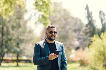 Stylish man in a blue suit in the city. Business style of emotion.Handsome Man in Suit is smiling Charmingly while browsing Internet on his Phone