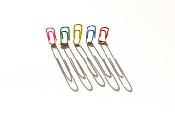 multicolored office paper clips and their shadows on a white background. Office and school supplies