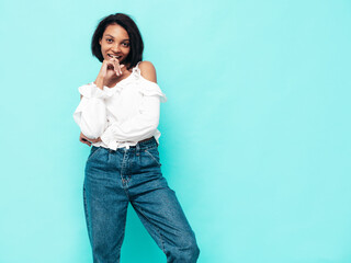 Portrait of young beautiful black woman. Smiling model dressed in summer jeans clothes. Sexy carefree female posing near blue wall in studio. Tanned and cheerful