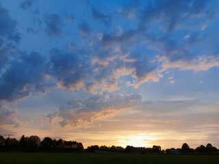 Fototapeta premium leuchtende Wolken in der Dämmerung rosa orange vor blauem Himmel mit Sonnenuntergang