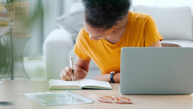 Serious, focused and smart student learning coding online, writing notes from her laptop in her notebook at home. Young college pupil concentrated on her IT computer study program at her house