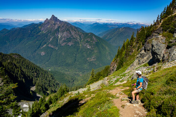 Fototapeta premium An adventurous athletic female hiker standing on a hiking trail in the Pacific Northwest looking out at a tall mountain.