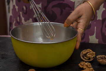 A lady whisking cake batter for making home made dry fruit cake with selective focus on walnut.