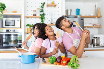 Cheerful young parents and little daughter having fun while baking together in kitchen, happy...