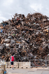 Tourist looking at huge pile of different scrap metal in a junk yard ready for export and transportation. Recycling industry.