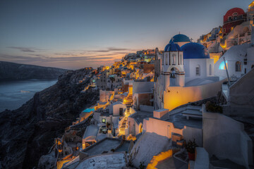 Scenic panoramic view of Oia village at sunset with the iconic blue domed church in the foreground, Santorini, Greece