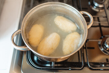 Traditional Lithuanian stuffed potato dumplings in the pot water. The dumplings are made from grated and riced potatoes and stuffed with ground meat.Indoors shot. © ARVD73