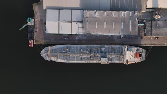 Petrochemical energy heavy transport industry cargo vessel tankers top down aerial drone view. Docked bulk carrier ship along storage facility silos. Energy gas and lpg petroleum commercial industry.