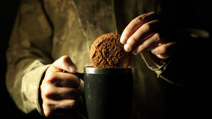 a soldier in a camouflage uniform soaks a cookie in a hot drink Field kitchen Making tea or coffee...