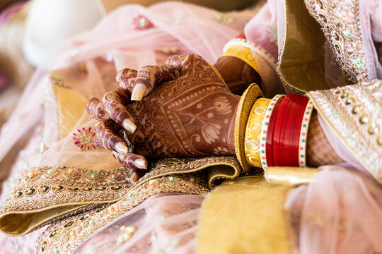 Beautiful Indian bride wearing red bangles and gold jewelry. Mehndi or Henna design on hands. New Indian bride at wedding.