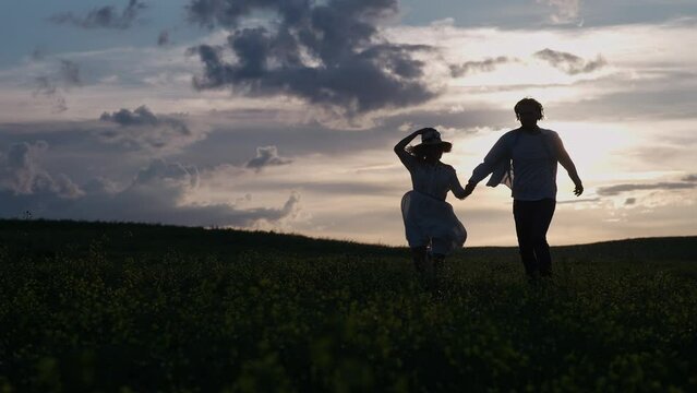 Countryside, cheerful couple rest in nature, man and a woman are running through a rapeseed field holding hands, contour lighting, 4k slow motion.