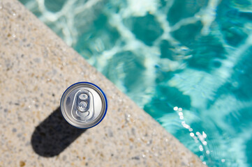 A can of cold drink by the pool in a hotel on a hot day. Top view, selective focus on the bank.