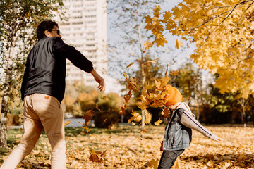 Father and son having fun in autumn park with fallen leaves, throwing up leaf. Child kid boy and...