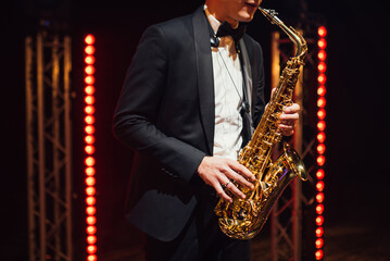 Obraz premium A saxophonist in a black suit plays on a stage with red lights. Jazz atmosphere.