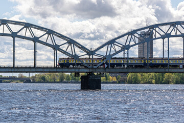 Naklejka premium The train rides on the railway bridge against the background of a cloudy blue sky.
