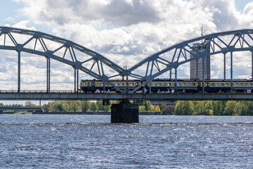 The train rides on the railway bridge against the background of a cloudy blue sky.