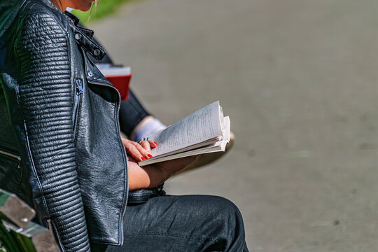 A Woman Sits On A Bench With A Book, Rests In A Sunny Autumn Green City Park In Nature.