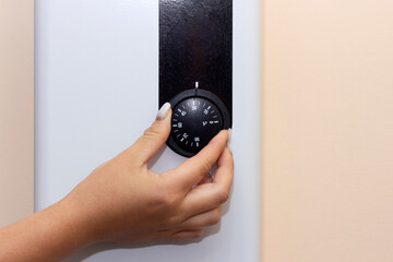 hand rotates temperature adjustment wheel, thermostat knob on gas boiler, gas saving concept