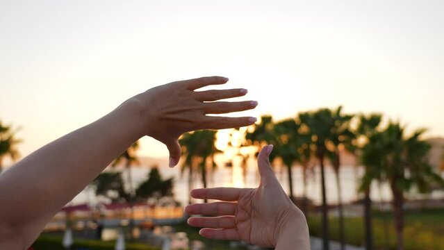 Closeup fpv 4k video footage of two female hands making frame or viewfinder sign gesture with her both hands isolated on sunny golden sunset or sunrise romantic tropical beach landscape background