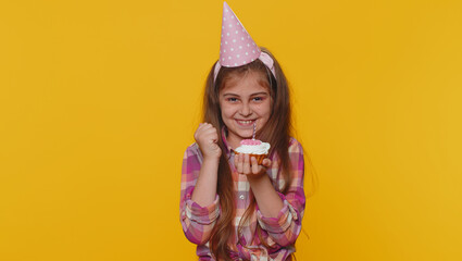 Happy young preteen child girl kid wears festive birthday hat hold cupcake makes wish joyful congratulating blowing burning candle on cake. Little toddler children celebrating anniversary party alone