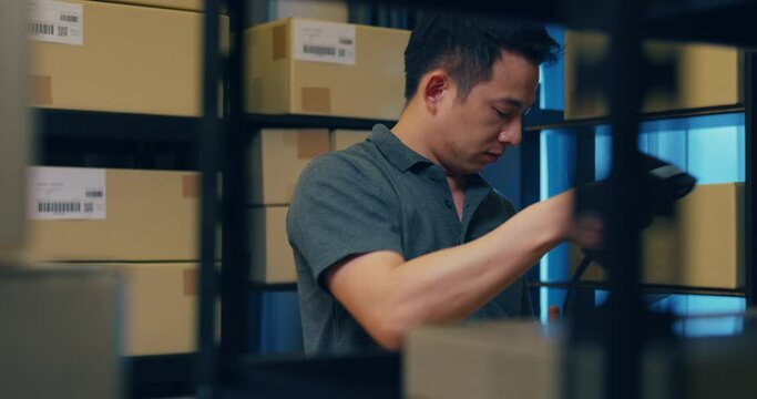 Asian businessman use barcode scanner scan paper box in shelf and put data in digital tablet cut stock online data information detail for express delivery at warehouse. Startup small business concept.