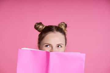 Close up of caucasian female teenager hidden behind pink  paper notebook