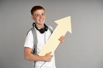 Redhead boy  with schoolbag looking at camera and holding big arrow
