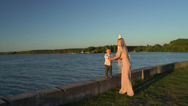 Caucasian Blonde In A Dress Leads a Child By The Hand Along The Pier