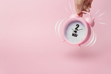 May 2nd. Day 2 of month, Calendar date. The morning alarm clock jumping up from the bell with calendar date on a pink background. Spring month, day of the year concept.