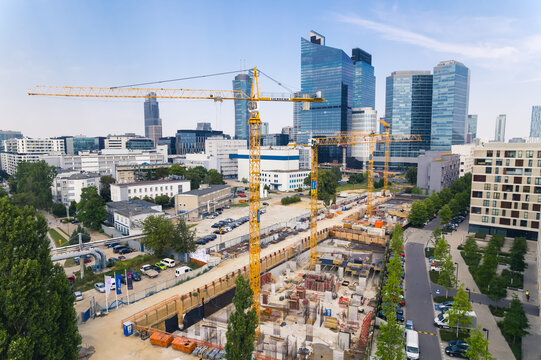 7.22.2022 Warsaw, Poland. Four yellow building cranes on vast construction site working on a new project. Skyscrapers in the background. New estate concept. High quality photo