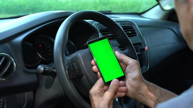 Chroma Key green screen smartphone in the car. An older man holds a green screen phone in his car