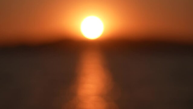 Blurry defocused sunset marine landscape. 4k video bokeh of orange defocused sun circle isolated on clear sky background, dark blurry sea waves in foreground. Abstract natural video background