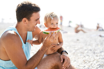 Smiling dad feeding little girl with watermelon on beach
