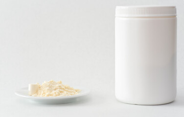Bovine colostrum powder with measuring scoop and white container on white background. Colostrum benefits for immune system and gut health concept