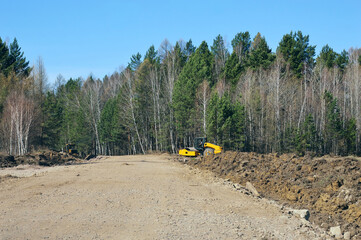 Heavy construction equipment is repairing a country road that runs through a dense forest. Sunny May day. Photographic project "Country roads".