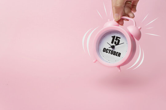 October 15th. Day 15 of month, Calendar date. The morning alarm clock jumping up from the bell with calendar date on a pink background. Autumn month, day of the year concept.