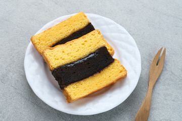 Spiku or Lapis Surabaya or Surabaya Layer Cake is a three-layer sponge cake with strawberry jam in between. Served in white plate, close up.
