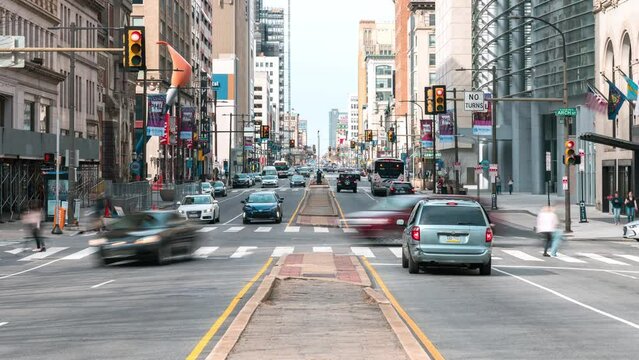 Downtown cityscape time-lapse of car traffic transportation, people walk cross road junction in Philadelphia, USA. Public transport, American city life, or commuter lifestyle concept. Zoom out
