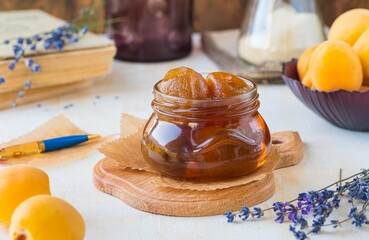 Apricot jam or apricots in syrup in a glass jar on a wooden board on a light concrete background. Vintage style.