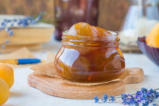 Apricot jam or apricots in syrup in a glass jar on a wooden board on a light concrete background. Vintage style.
