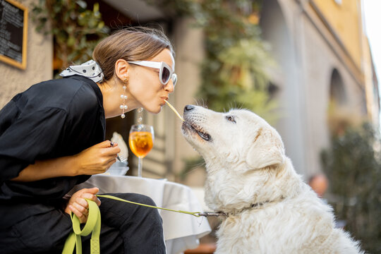 Woman eating pasta with her cute white dog at the restaurant outdoors. Concept of friendship with pets and having fun together