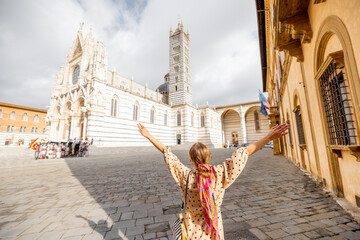 Woman enjoys beautiful architecture of Siena cathedral, standing back on Duomo square in Siena town. Traveling old towns of Tuscany region of Italy. Woman wearing colorful shawl in hair