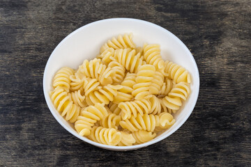 Boiled spiral pasta in the bowl on a black surface