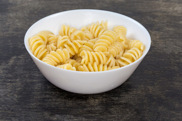 Boiled spiral pasta in bowl on black surface close-up