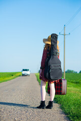 Woman with guitar hitchhiking on the empty road on a sunny summer day