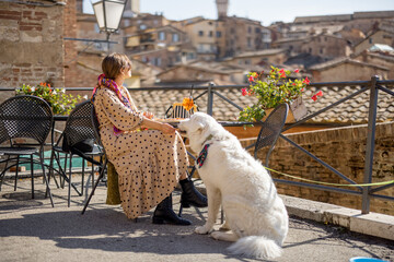Woman feeds her dog while sitting at restaurant with beautiful view on Siena town. Traveling...