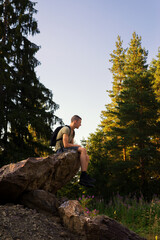 Young man sitting in the rock in the nature on a sunny summer day