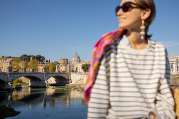 Woman enjoying beautiful view of Rome city and Vatican standing on the bridge on a sunny autumn day. Elegant woman wearing stripped blouse and shawl in hair. Focus on background