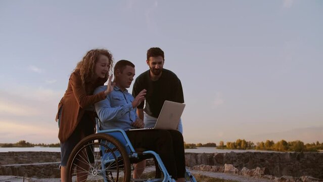 disabled man and his friends are on a video call with his family. A man in a wheelchair holds a laptop and shows his friends his projects.A company of friends spend time together.